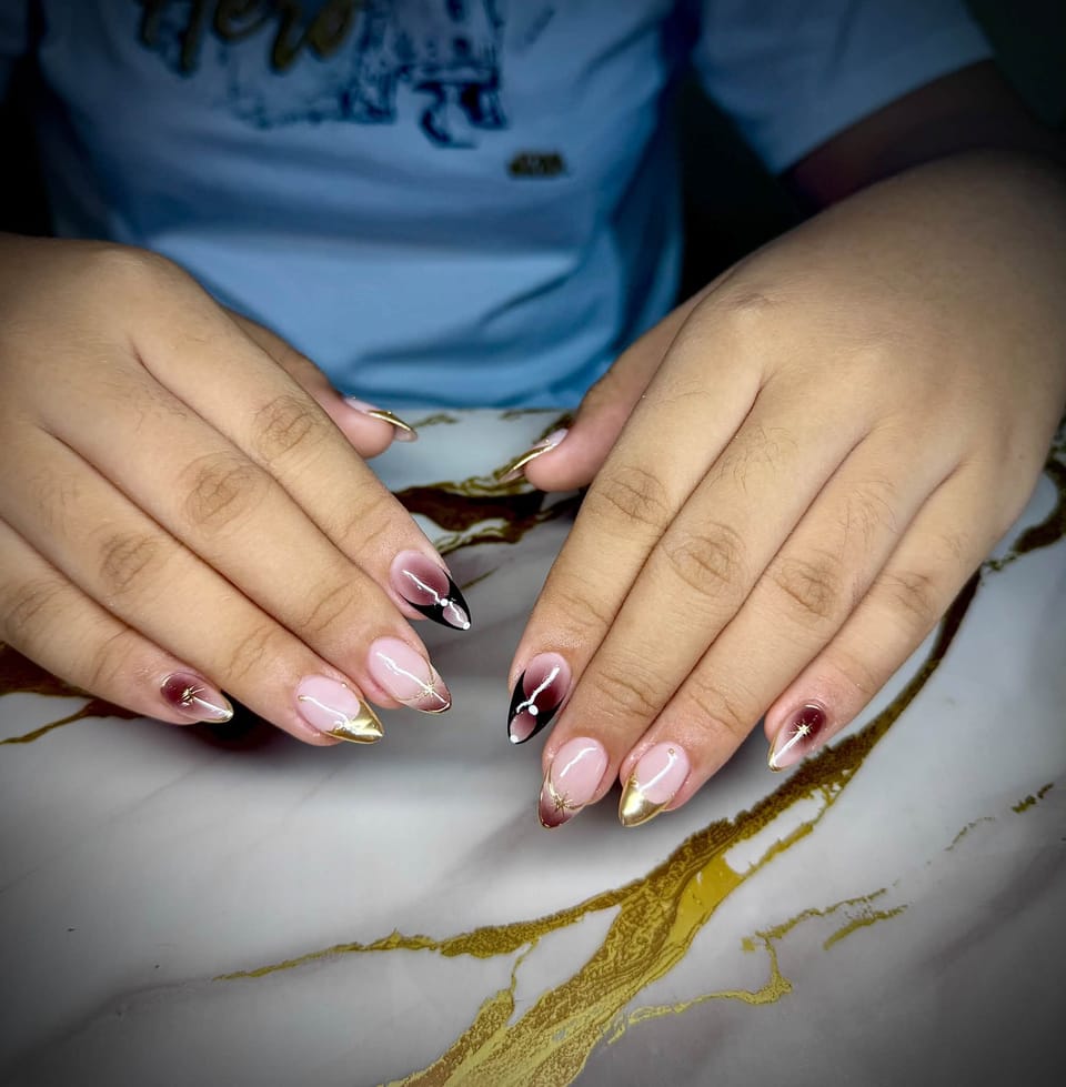 Pink almond nails with black gradient and gold tips, fine white lines and tiny gold stars.