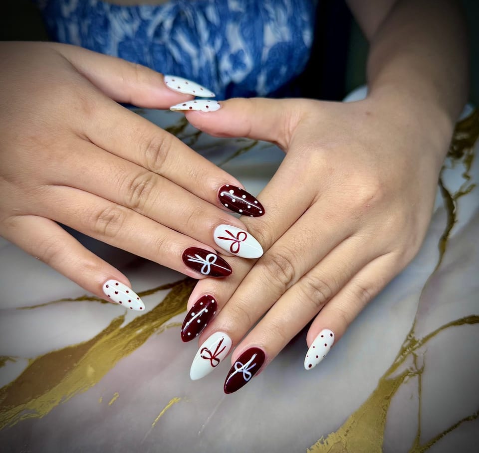 Almond nails alternating deep burgundy and white with painted bows and polka dots.