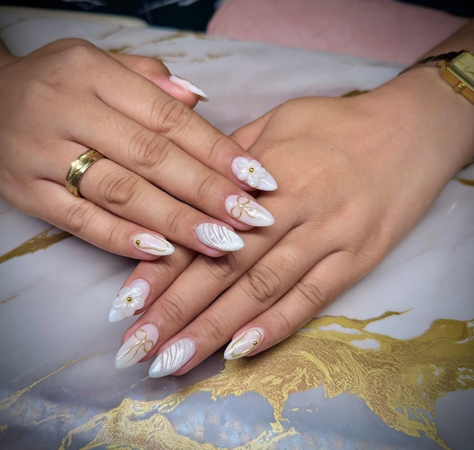 Pearly white almond nails with raised white flowers and fine gold bow outlines.
