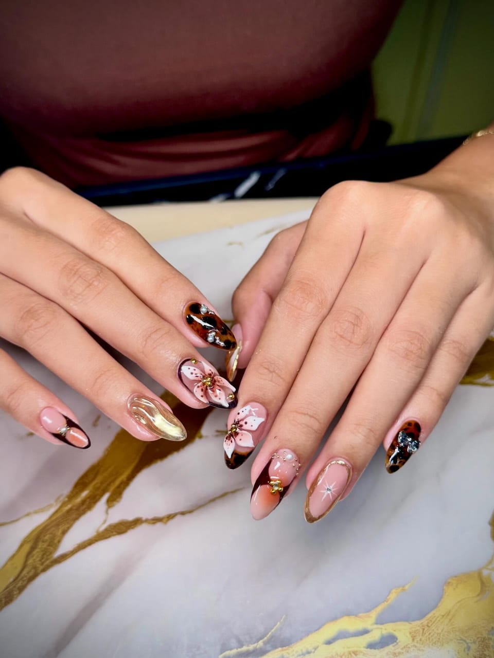 Almond nails mixing tortoiseshell, a hand-painted lily, chrome gold and small gems.